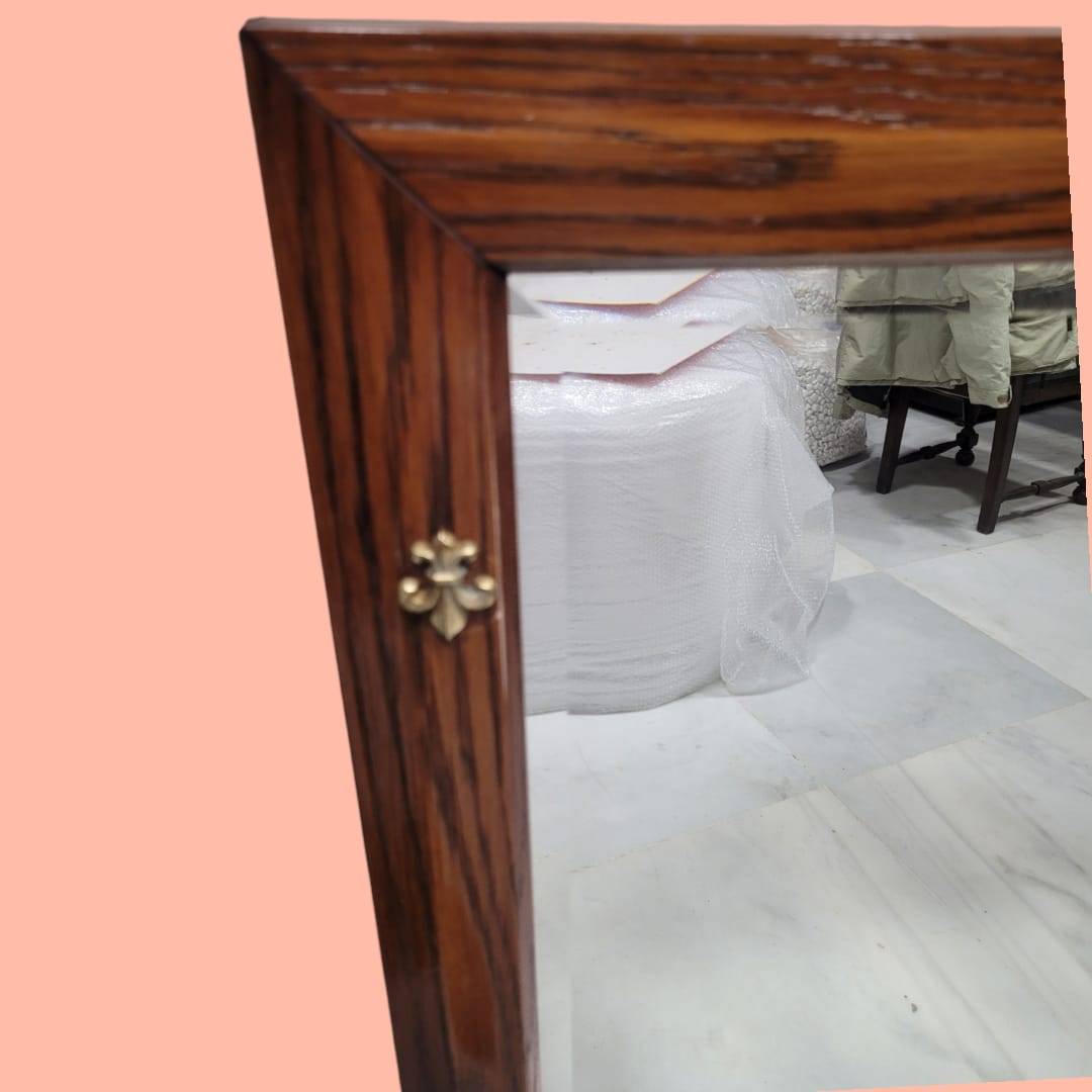 Detalle del marco de madera con veta visible y adorno metálico, parte del espejo de madera con cristal biselado para decoración del hogar.