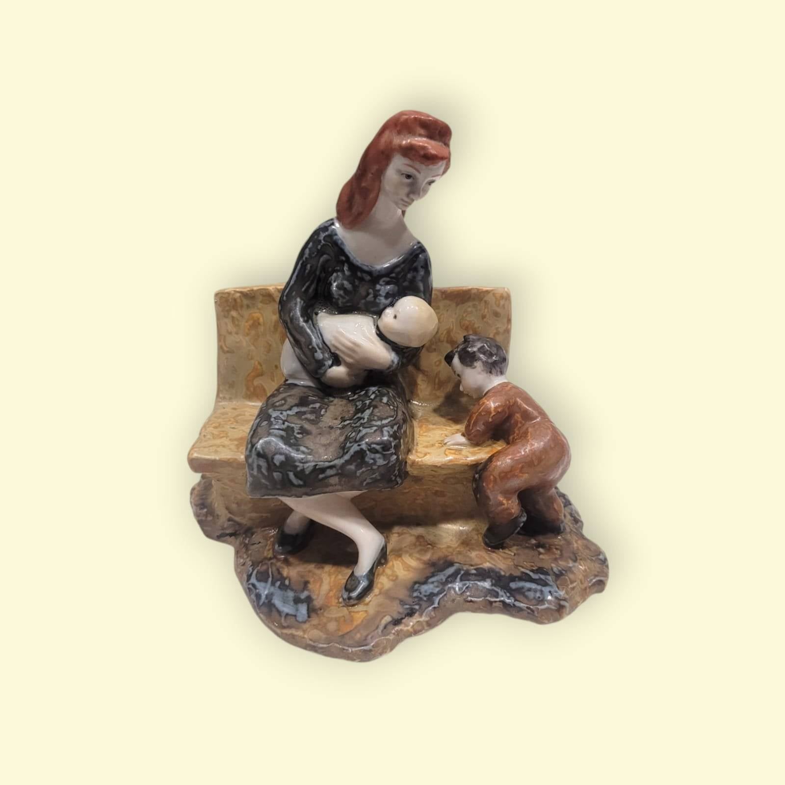 Figura de Porcelana Valenciana Nalda: madre amamantando a su bebé en un banco con niño pequeño al lado, decoración artesanal emotiva.