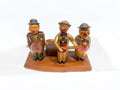 Detalle frontal de figuras de madera tallada con temática musical, integradas con caja de música y accesorios para vino.