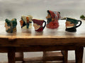 Set de jarras Royal Doulton con figuras históricas sobre mesa rústica frente al mar, decoración temática para hogar o jardín.