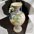 Ánfora de cerámica de Talavera con asas ornamentadas y escenas paisajísticas pintadas a mano. Pieza artesanal perfecta para decoración clásica.