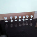 Siete copas de licor de cristal tallado antiguo alineadas sobre superficie negra, perfectas para coleccionistas y decoración elegante.