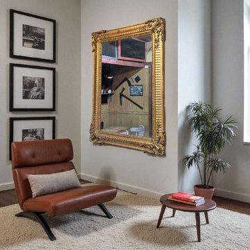 Espejo romántico antiguo con marco de pan de oro original colgado en pared blanca, reflejando interior elegante con decoración clásica.