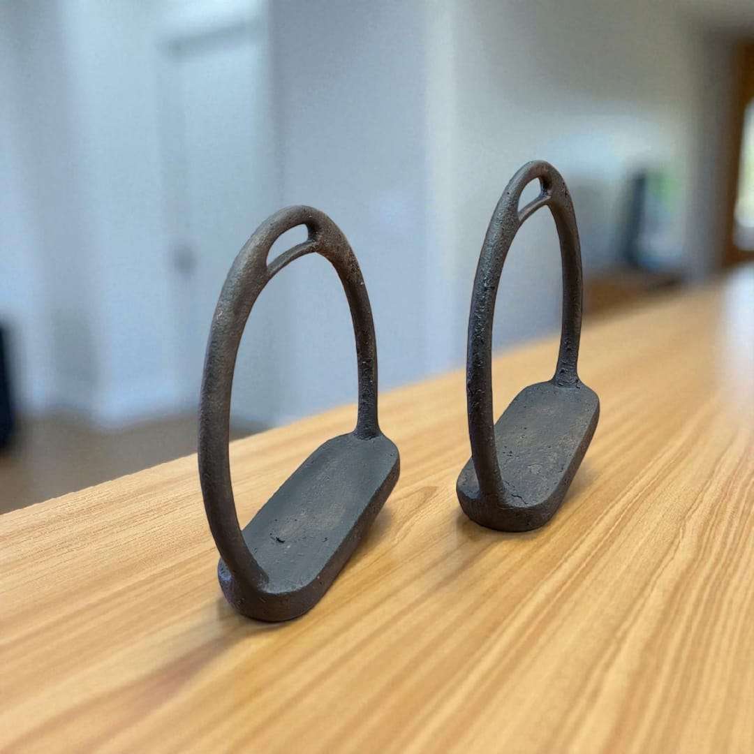 Estribos antiguos de hierro sobre mesa de madera junto a planta