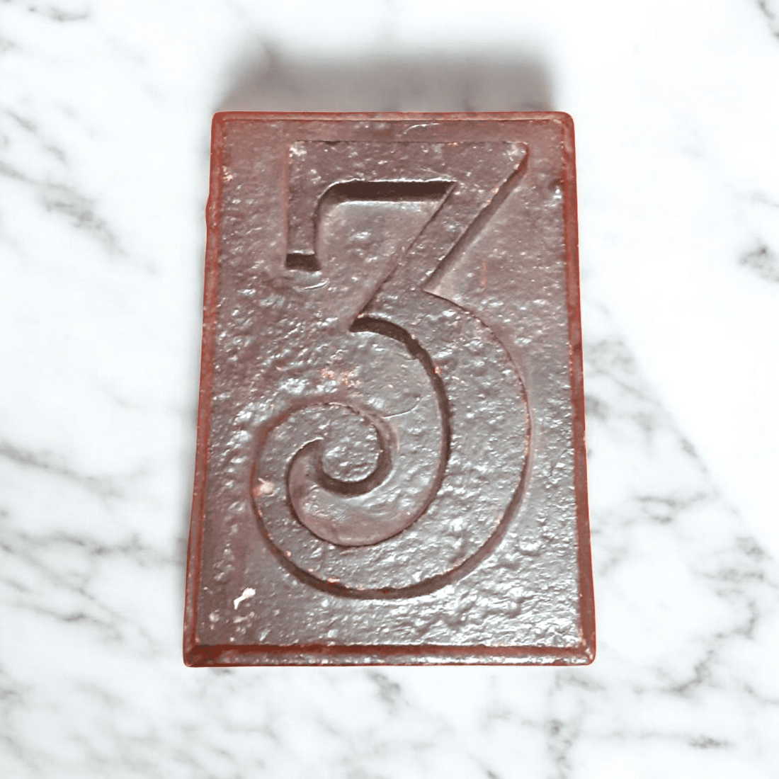 Número 3 de hierro fundido vintage con acabado rústico sobre fondo de mármol. Decoración única y resistente para exteriores o interiores.