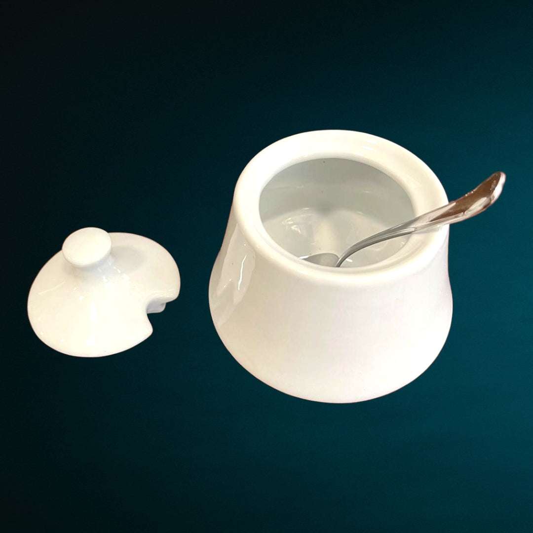 Azucarero en porcelana blanca abierto con tapa removida y cuchara incluida, perfecto para coleccionistas y decoración de mesa refinada.