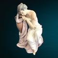 Figura Lladró 'Soñando Despierta' en porcelana fina, muestra a mujer recostada sobre ánfora con vestido blanco y rosa. Ideal para decoración elegante.