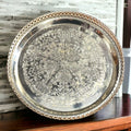 Bandeja Decorada de metal plateado con detalles grabados y borde calado. Perfecta para decoración elegante en el hogar, 23xH4 cm.