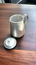 Jarra de aluminio vintage de 1/2 litro con tapa desmontada sobre mesa de madera. Perfecta para añadir estilo rústico a la decoración del hogar.