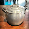 Olla de Aluminio Vintage con asas negras sobre mesa de madera, ideal para decoración rústica de cocina. Tradición y elegancia para tu hogar.