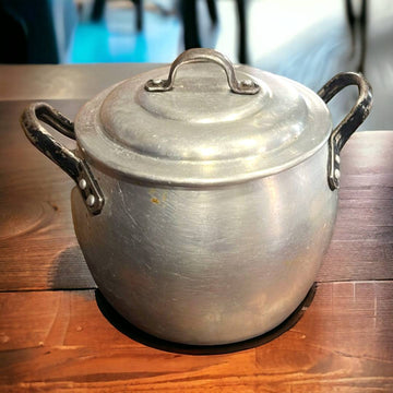 Olla de Aluminio Vintage con asas negras sobre mesa de madera, ideal para decoración rústica de cocina. Tradición y elegancia para tu hogar.
