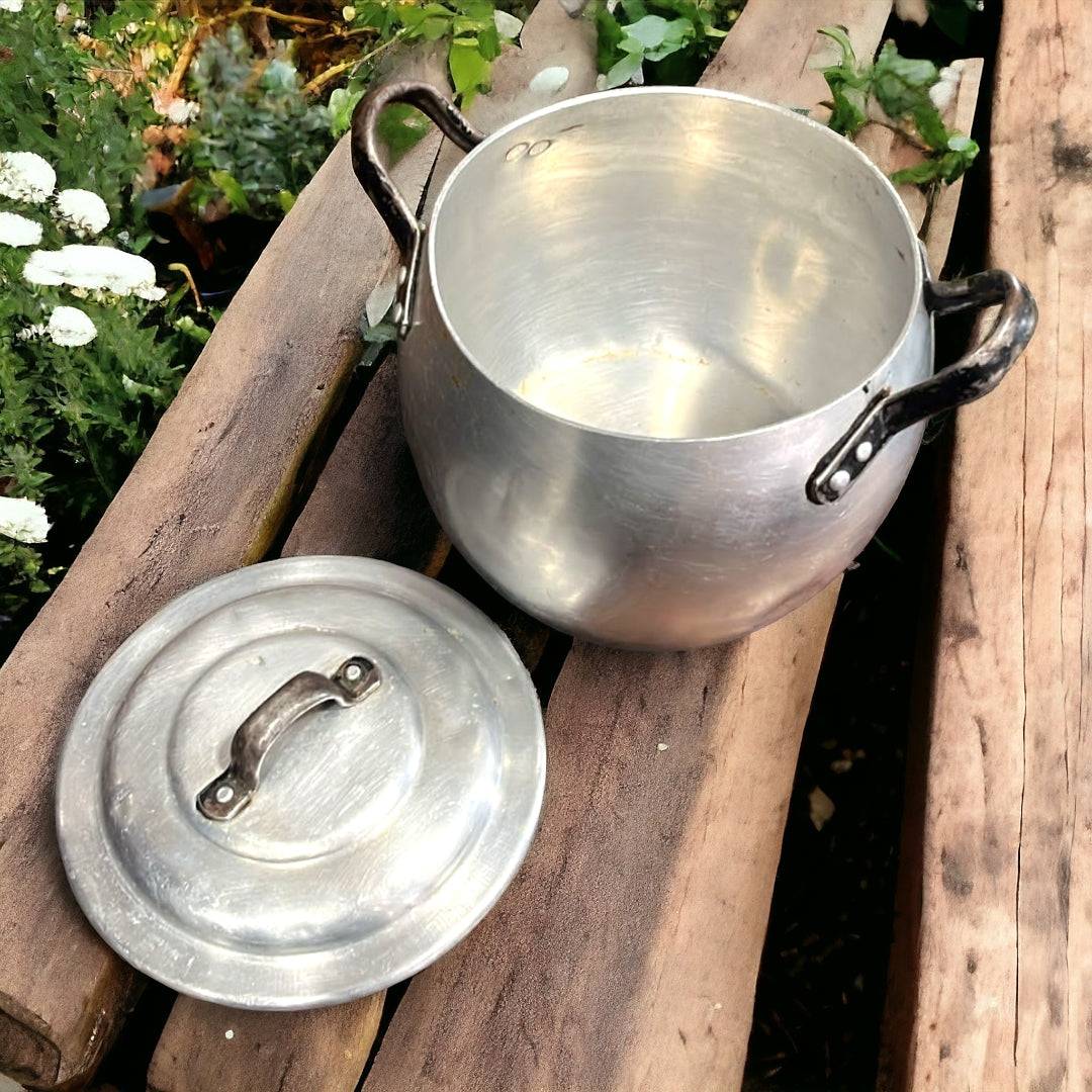 Olla de Aluminio Vintage abierta con tapa al lado, colocada sobre troncos en jardín. Perfecta para decoración de estilo retro en exteriores.