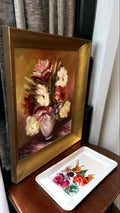 Decoración de interiores con Óleo Floral de R. Naher - Arte Exquisito para Tu Hogar, enmarcado en dorado y colocado sobre mesa de madera.