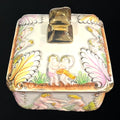 Vista superior de la bombonera de porcelana con tapa decorada con figuras en relieve y detalles dorados. Diseño elegante para decoración y almacenamiento.