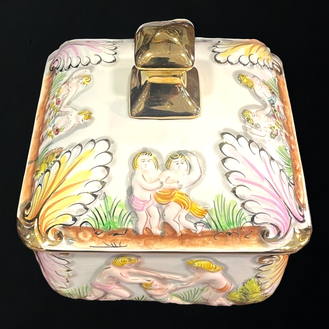 Vista superior de la bombonera de porcelana con tapa decorada con figuras en relieve y detalles dorados. Diseño elegante para decoración y almacenamiento.