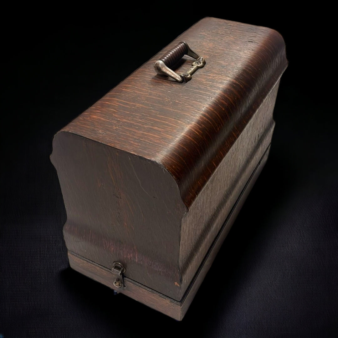 Caja de madera antigua con asa metálica, diseñada para transportar y proteger la máquina de coser portátil New Ideal de 1846.