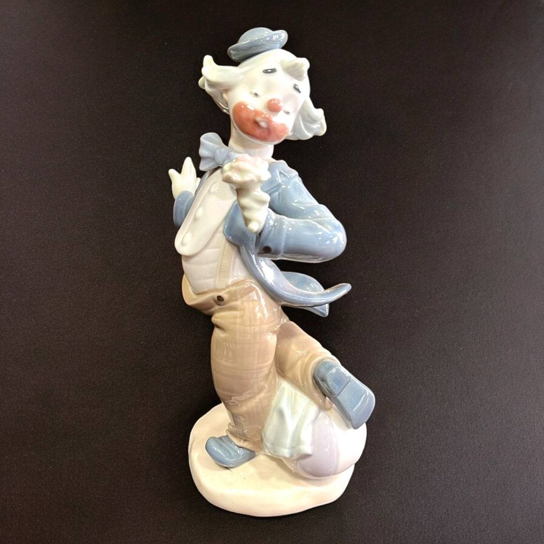 Figura de porcelana Nao-Lladró de payaso con flor en mano, vestimenta azul y beige, pieza decorativa de alta calidad artesanal.