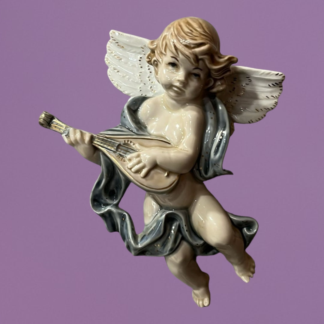 Ángel músico de porcelana tocando un laúd, con alas blancas y detalles refinados, sobre fondo lila. Arte decorativo para pared.