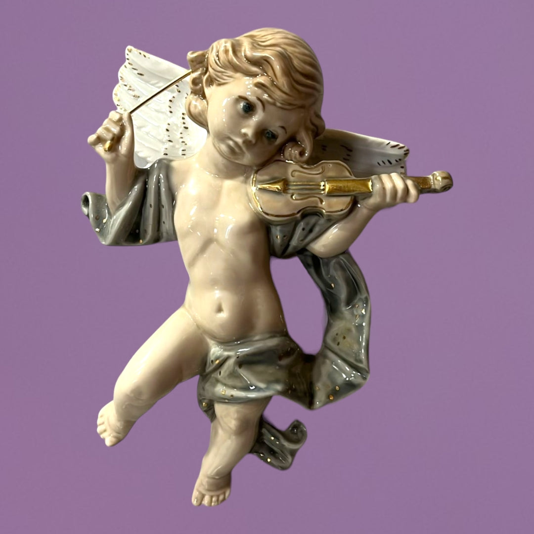 Ángel músico de porcelana tocando un violín, con alas blancas y diseño elegante, sobre fondo lila. Perfecto para decoración de pared.