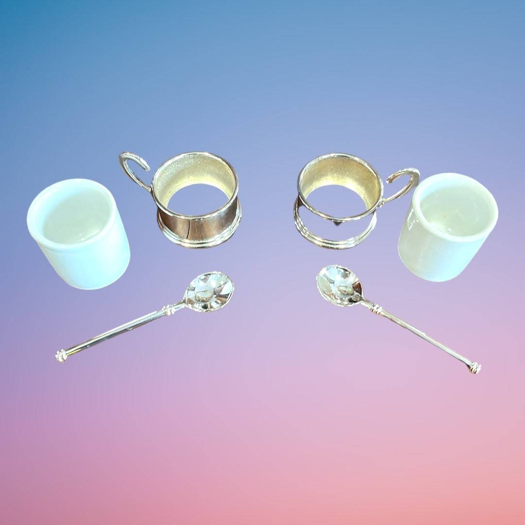 Set de tazas de té Terno Siglo XX desmontado, mostrando tazas de porcelana blanca, bases de acero y cucharas decorativas.