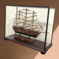 Maqueta artesanal del velero Cutty Sark en urna de cristal con fondo marrón. Pieza decorativa para amantes de barcos antiguos.