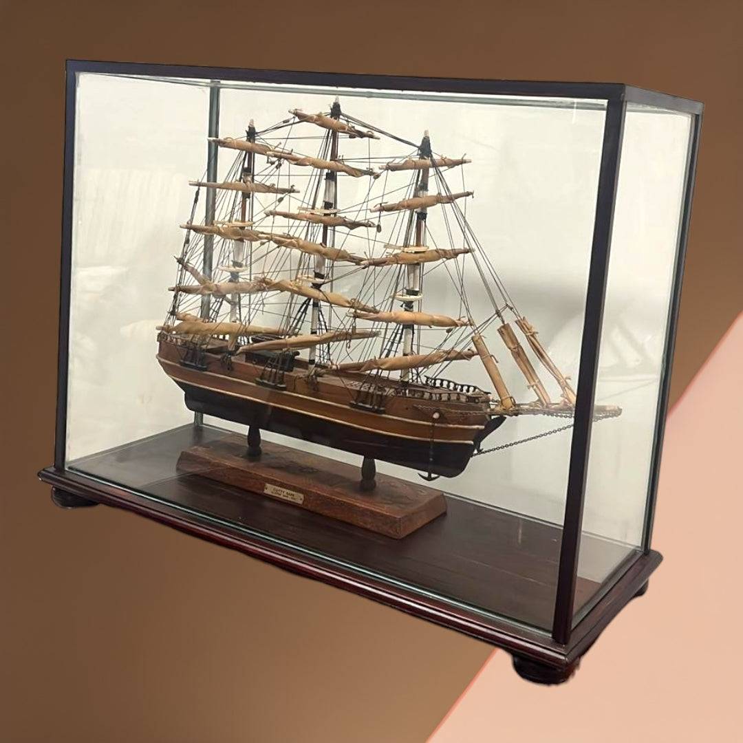 Maqueta artesanal del velero Cutty Sark en urna de cristal con fondo marrón. Pieza decorativa para amantes de barcos antiguos.