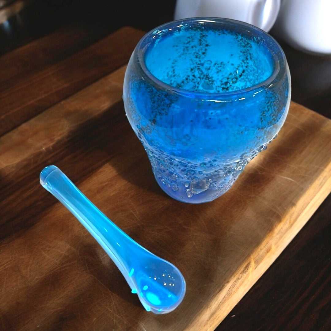 Mortero de cristal de Murano azul con mano a juego sobre tabla de madera, pieza única para decoración en hogar o regalo artesanal.