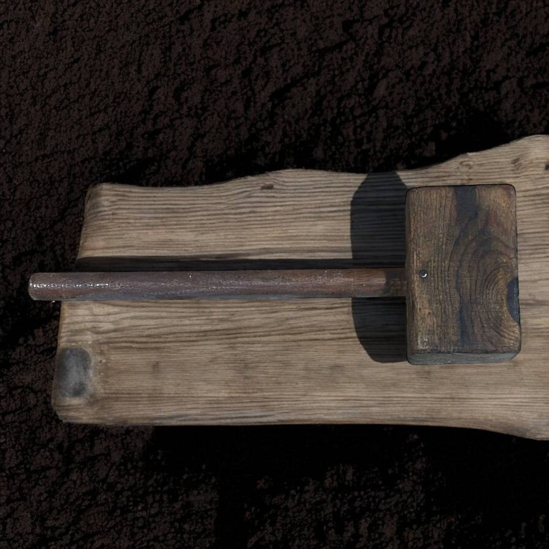 Antiguo mazo de madera rústico colocado sobre tabla envejecida, perfecto como elemento decorativo artesanal en espacios de estilo rústico.