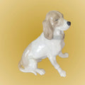 Figura decorativa de porcelana de perro Cocker en posición sentada, con expresión serena y orejas caídas. Pieza de colección refinada.