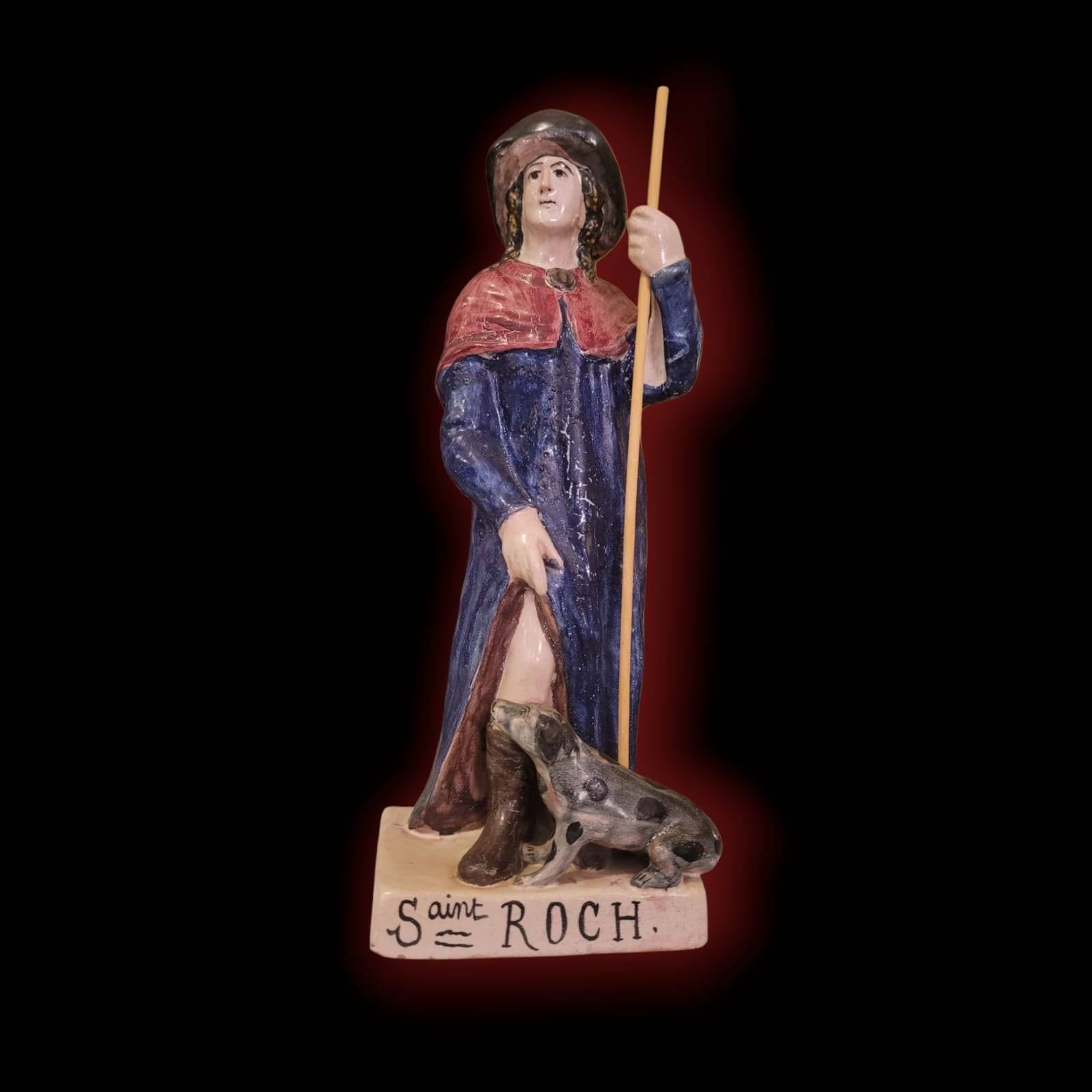 Figura frontal de San Roque en terracota esmaltada con perro, bastón y base con inscripción. Decoración artesanal disponible en Cositas Antiguas.