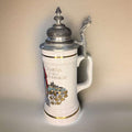 Jarra de cerveza alemana de porcelana con tapa metal grabada y texto en latín, diseño decorativo con castillo y detalles dorados. Ideal para colección en decoración de hogar.