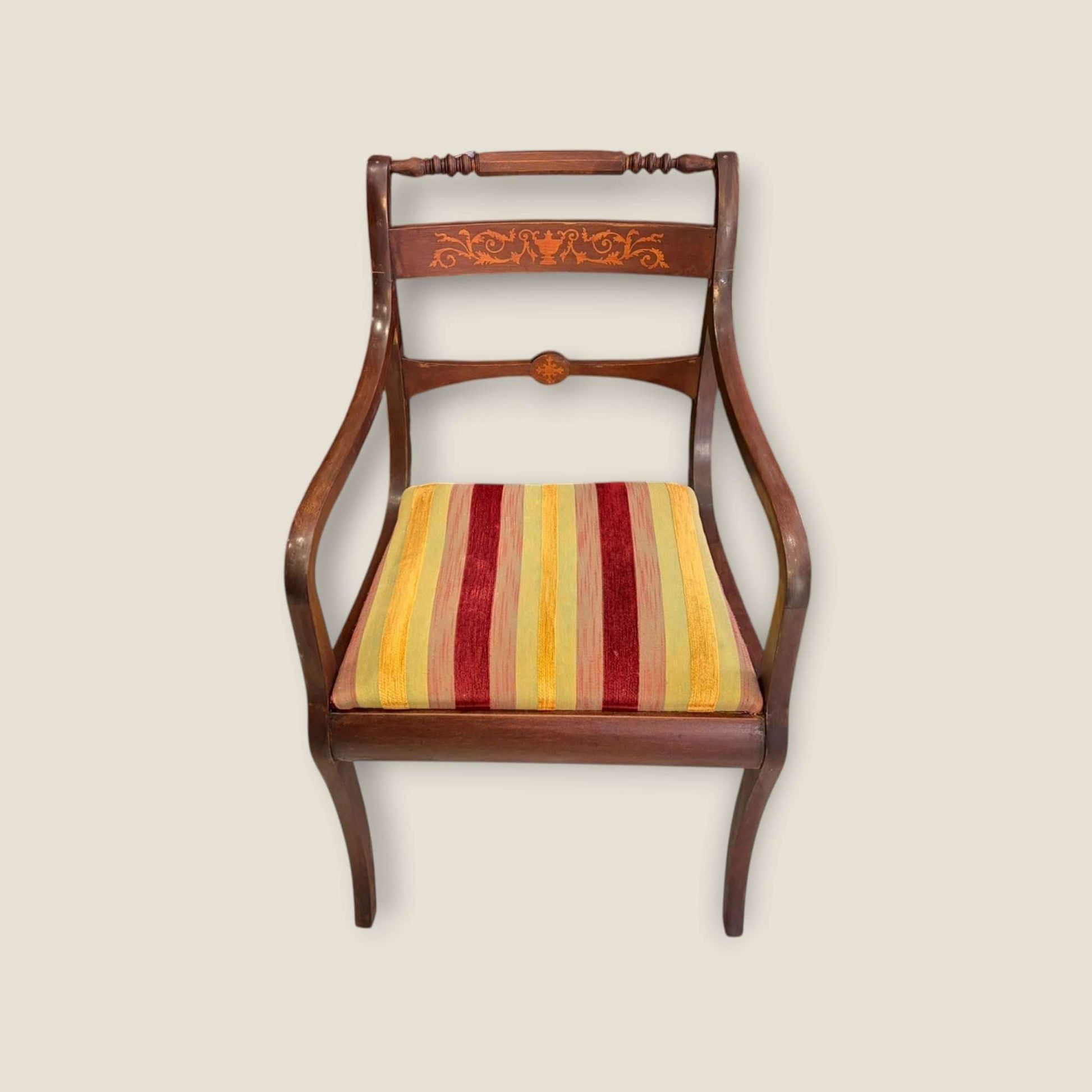 Sillón de caoba con detalles de taracea y brazos elegantes, asiento acolchado con tela a rayas rojas y amarillas. Estilo clásico para interiores refinados.