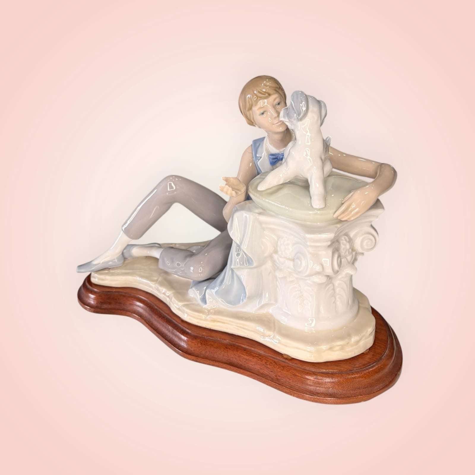 Escultura Nao Lladró de porcelana esmaltada mostrando a un niño con perro sobre columna clásica, pieza decorativa de alta calidad para interiores.