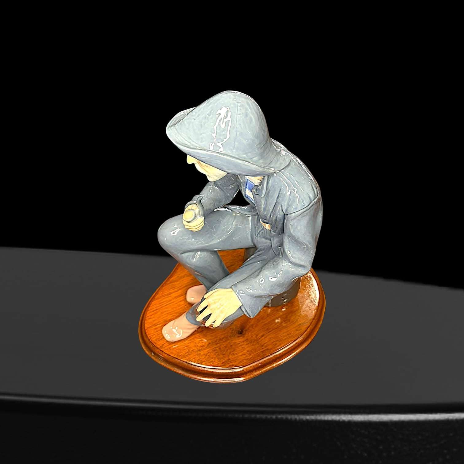 Vista superior de figura Lladró marinero fumando pipa, con chaqueta y sombrero, sentado sobre base de madera. Pieza decorativa artesanal de colección.