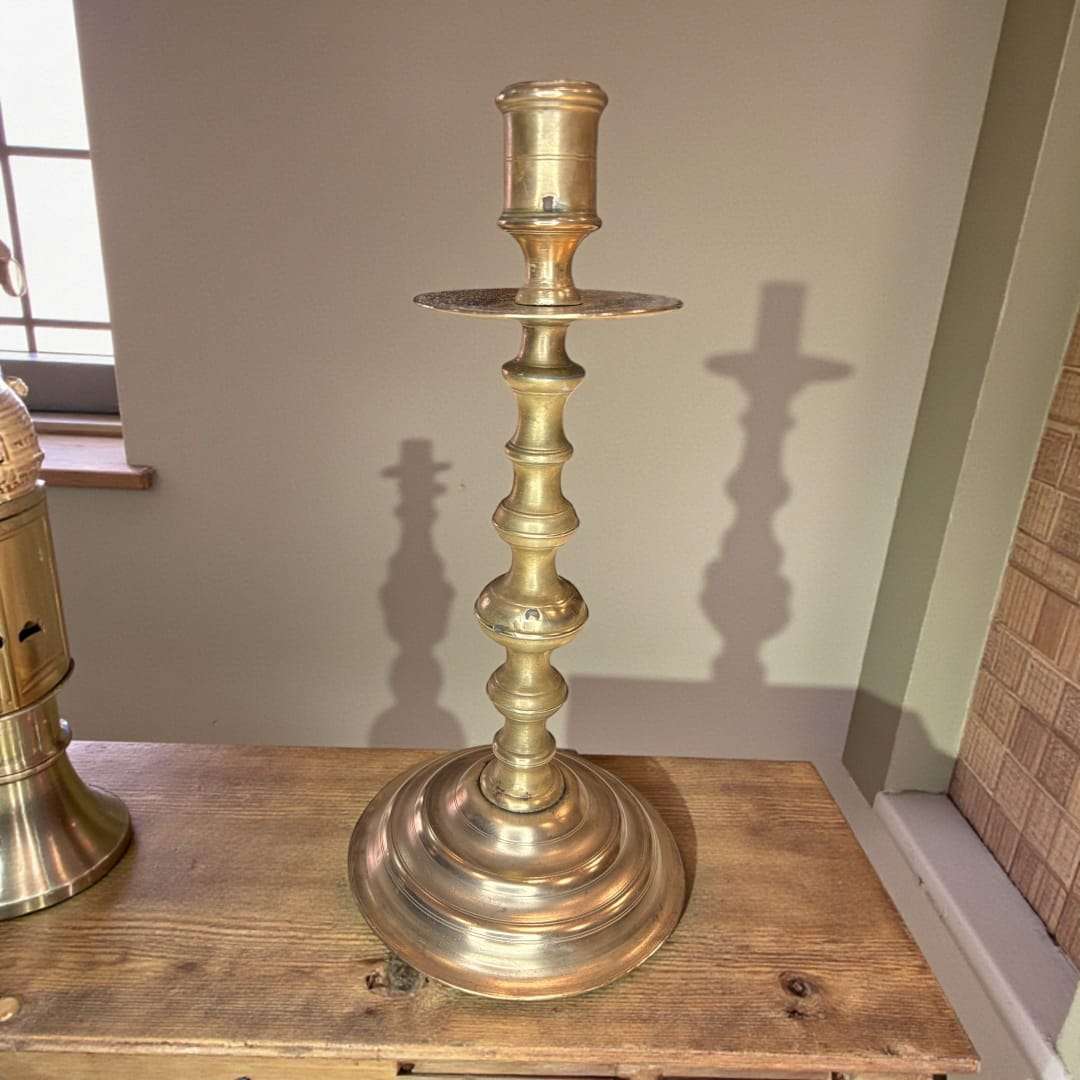 Candelabro antiguo de metal dorado con base ancha, colocado en mesa de madera junto a ventana, perfecto para decoración vintage.