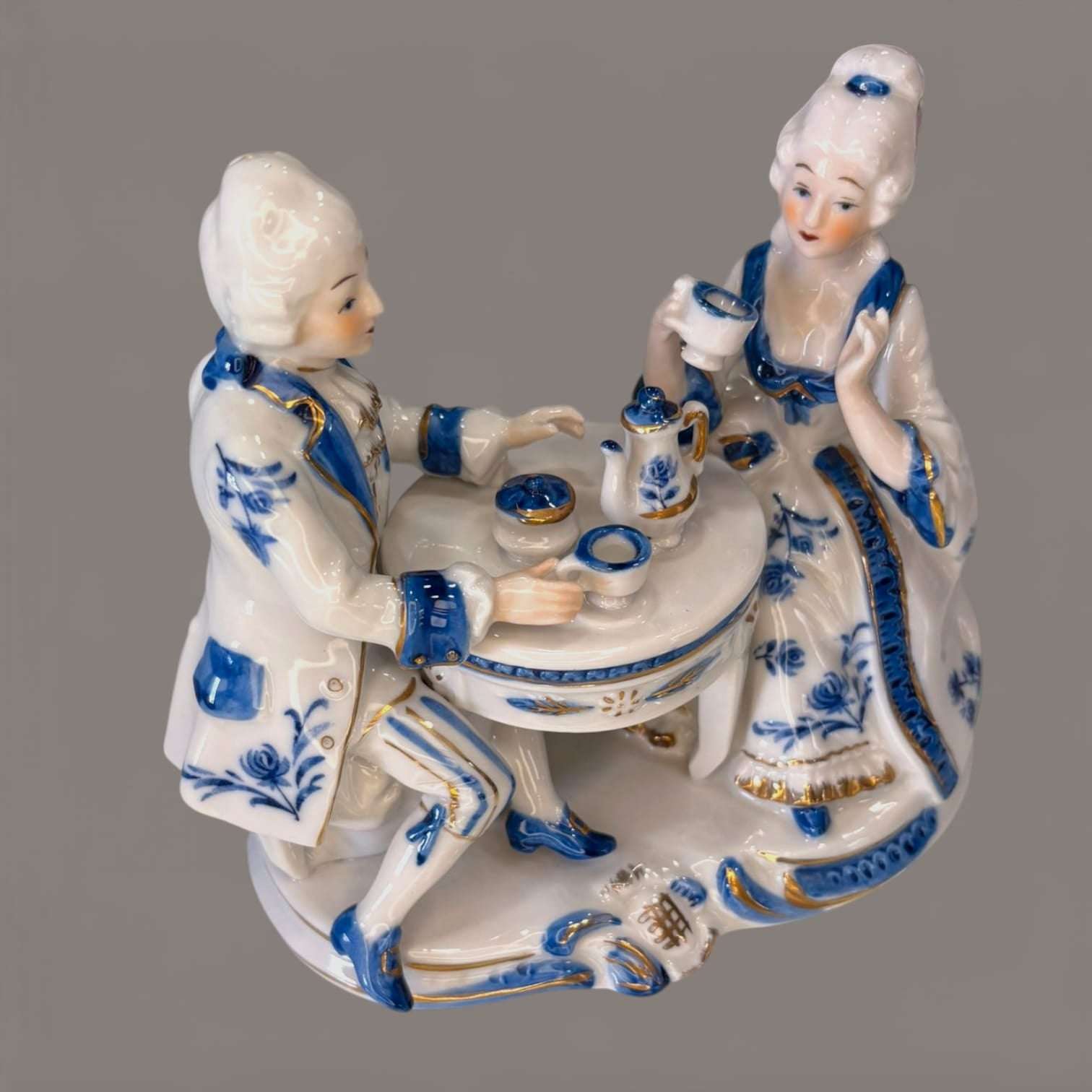 Decoración de porcelana azul y blanca estilo victoriano con pareja sentada en mesa de té, ideal para coleccionistas de figuras vintage.