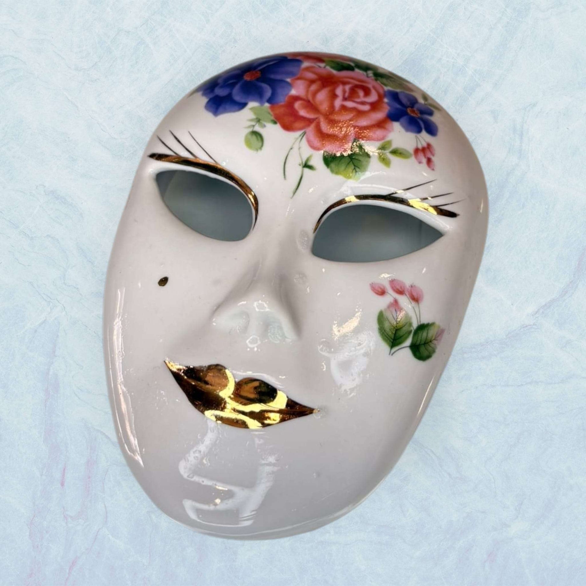 Máscara de porcelana veneciana Galos y Ocer única con flores pintadas a mano y labios dorados, ideal para decoración artística de interiores.