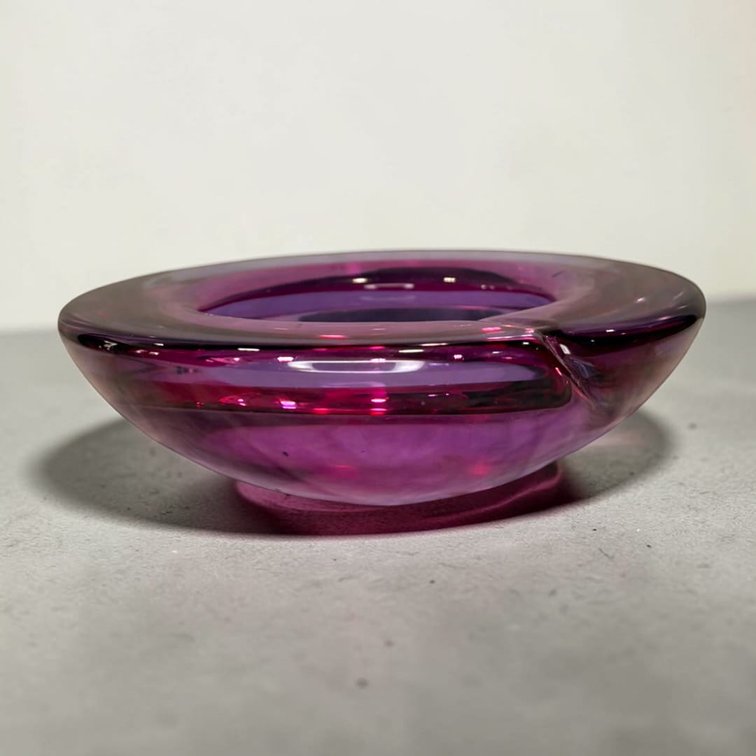 El Cenicero de cristal Murano violeta es una pieza decorativa que combina la funcionalidad cotidiana con la belleza del cristal artístico.
