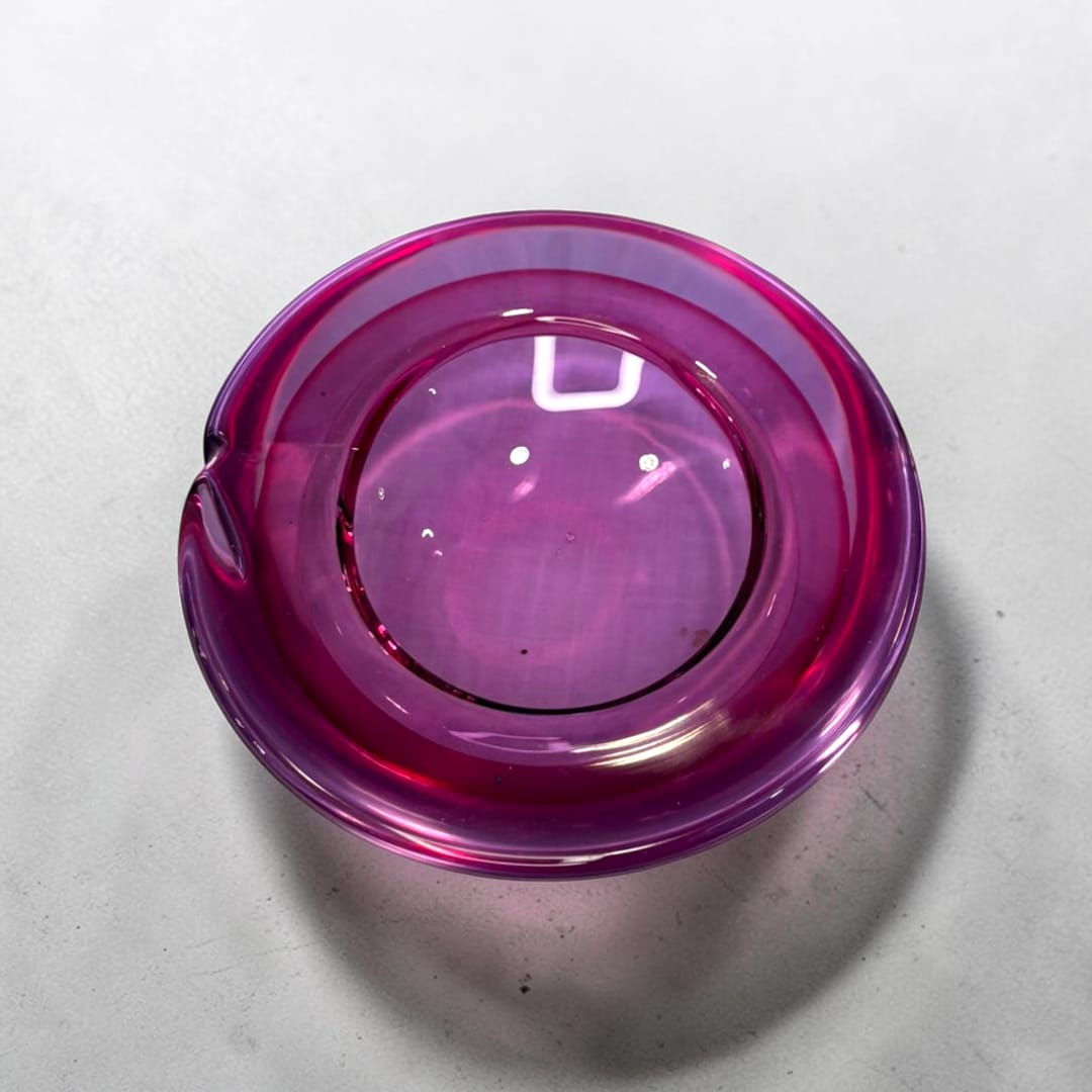 Este Cenicero de cristal Murano violeta presenta una forma circular de líneas suaves y equilibradas, con un cuerpo de cristal macizo y pulido que refleja la luz creando matices y reflejos muy atractivos.