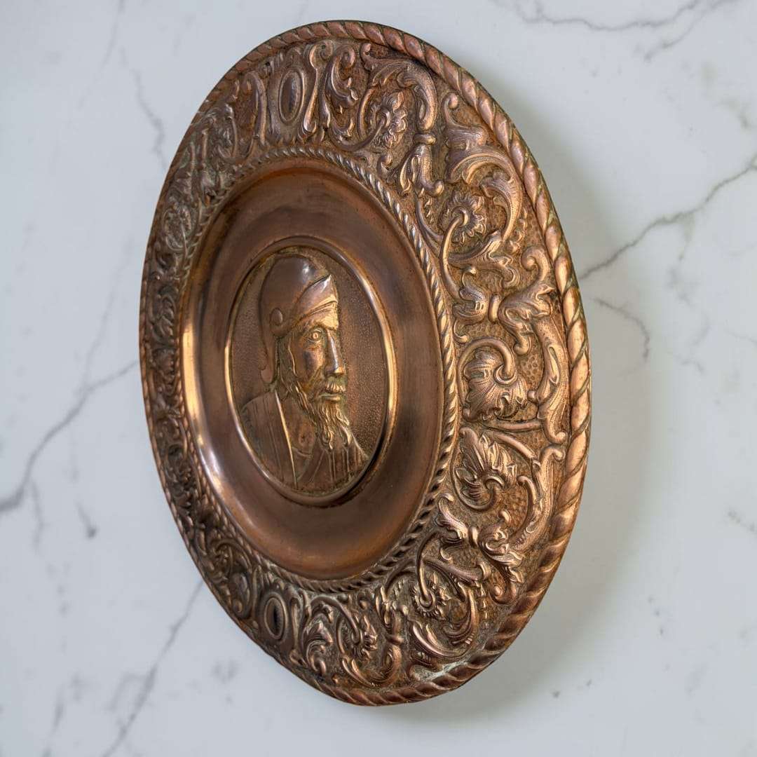 En uno de los platos aparece el busto en relieve de un hombre de perfil, con apariencia de soldado o personaje de inspiración clásica, mientras que en el otro se aprecia el rostro femenino de perfil, ambos enmarcados por un ala ricamente ornamentada con roleos, volutas y motivos vegetales. 
