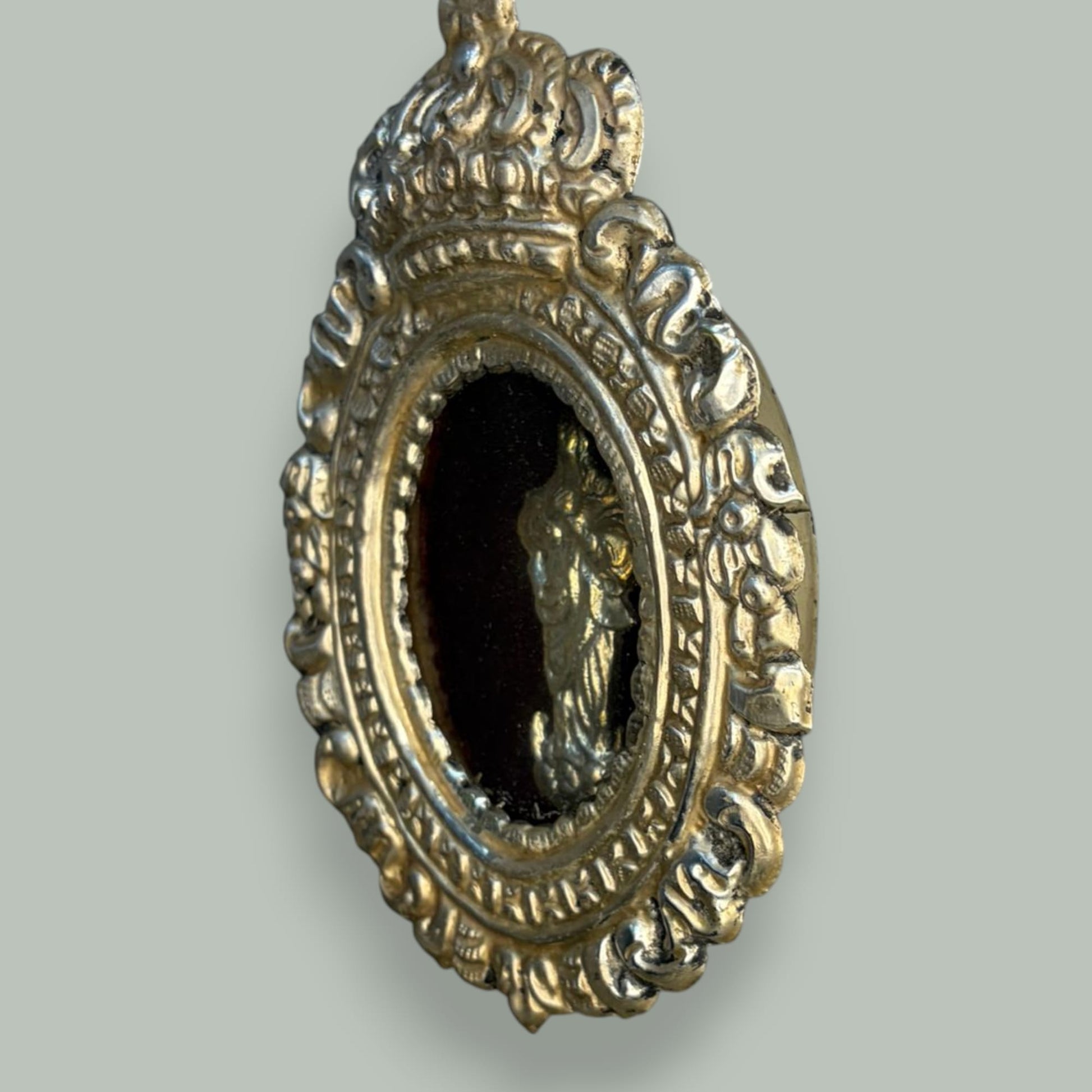 Lo que hace especialmente atractivo este relicario de metal plateado con imagen de la Virgen es la riqueza ornamental que se aprecia en las fotografías.