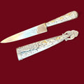 Pieza antigua de carácter decorativo y de colección, compuesta por daga y funda a juego en metal plateado. Presenta una estética muy ornamental, con abundantes relieves y una composición visual especialmente cuidada. 
