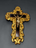 Se trata de una figura de Jesucristo crucificado tipo Olot, colocada sobre una cruz de caoba de tono oscuro y enmarcada por un espectacular contorno ornamental dorado tallado en madera. 