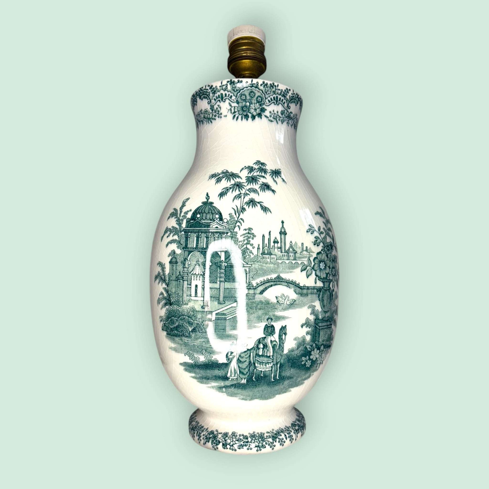  El cuerpo de loza muestra una decoración en tono verde sobre fondo marfil, con una escena paisajística de gran encanto: arquitectura clasicista, puente, vegetación, figuras y una composición inspirada en paisajes románticos y orientales, muy característica de la cerámica decorativa histórica