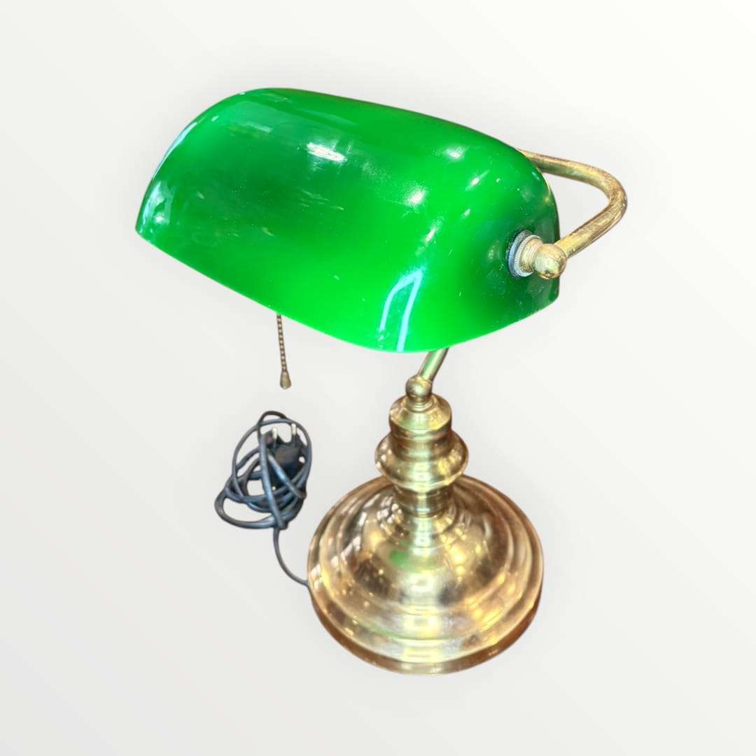 Su pantalla curva en tono verde intenso, combinada con una base metálica dorada de perfil torneado, crea una pieza con alma vintage, ideal para despachos, bibliotecas, estudios, recepciones o rincones de lectura. La silueta recuerda al universo de las lámparas de banquero, muy apreciadas en decoración por su elegancia sobria y