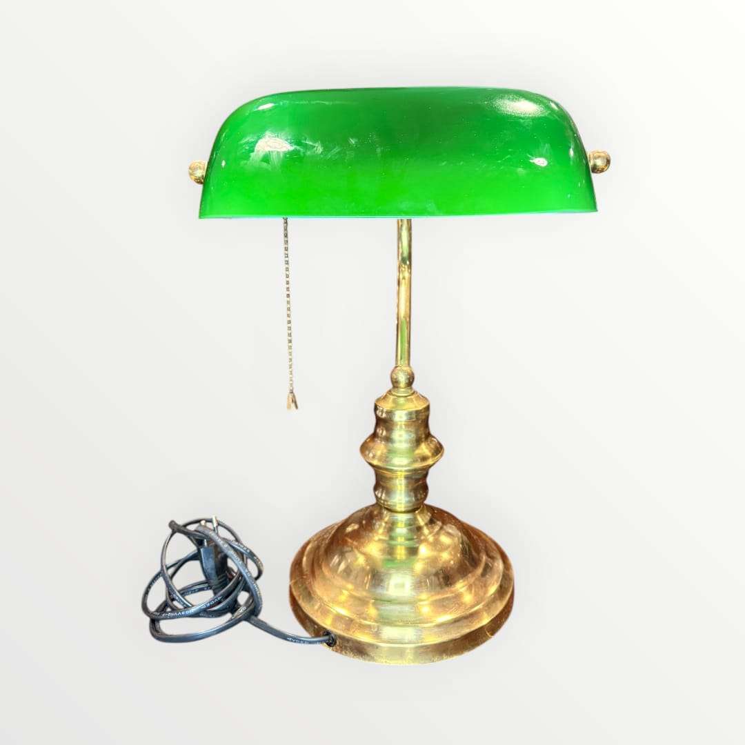  Su pantalla curva en tono verde intenso, combinada con una base metálica dorada de perfil torneado, crea una pieza con alma vintage, ideal para despachos, bibliotecas, estudios, recepciones o rincones de lectura. La silueta recuerda al universo de las lámparas de banquero, muy apreciadas en decoración por su elegancia sobria y