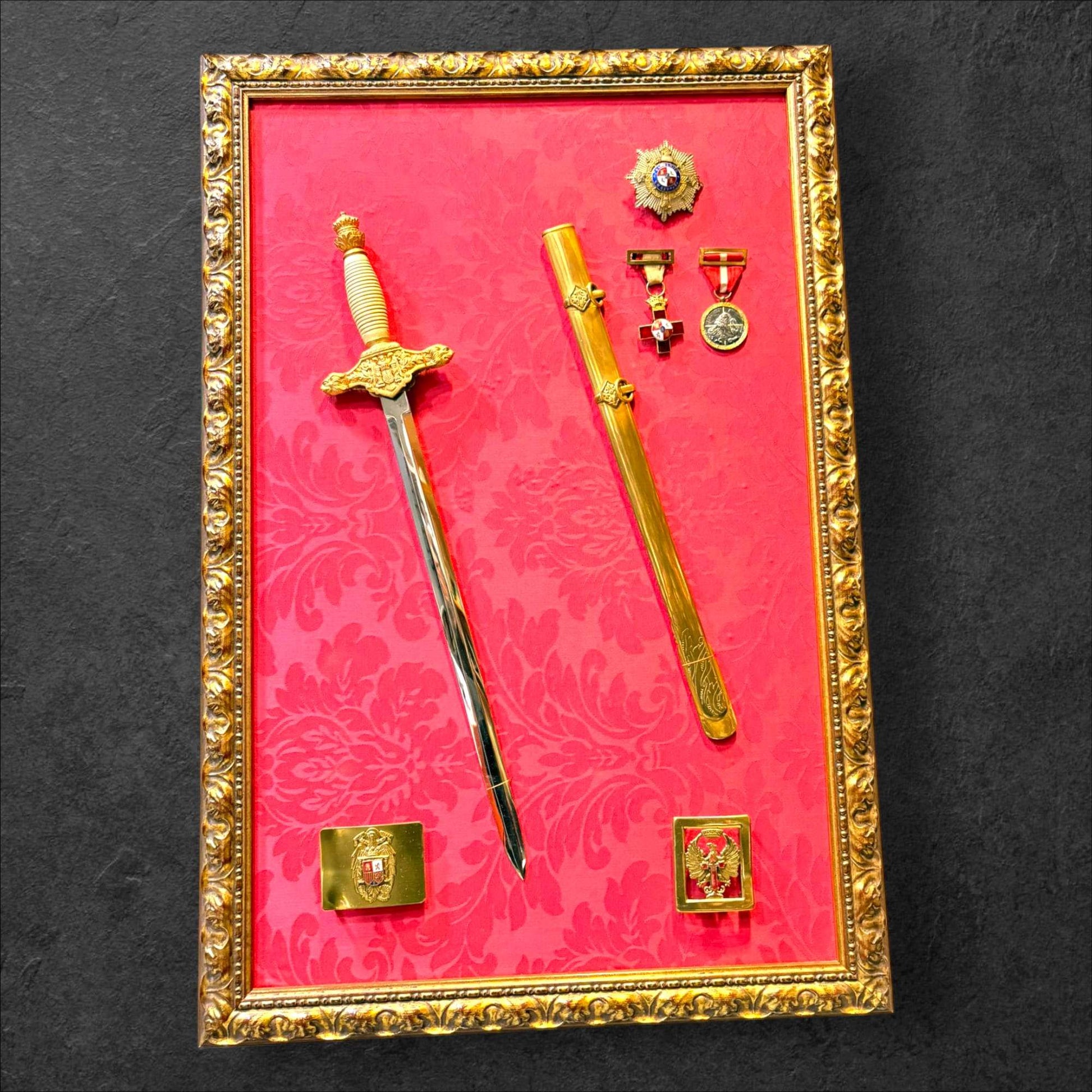 En su composición destaca una daga militar española con vaina, acompañada por medallas, insignias y elementos conmemorativos colocados sobre un fondo rojo ornamentado.

