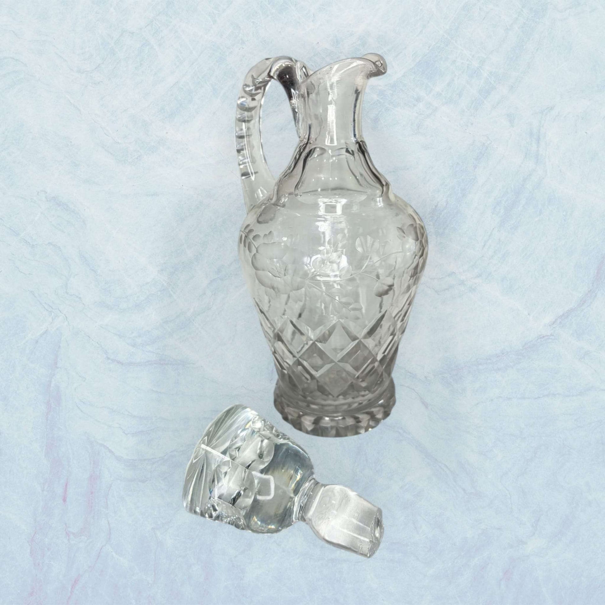 Su diseño con asa, pico vertedor y tapón de cristal refleja el gusto por los servicios de mesa cuidados, donde cada detalle aportaba presencia y distinción.
