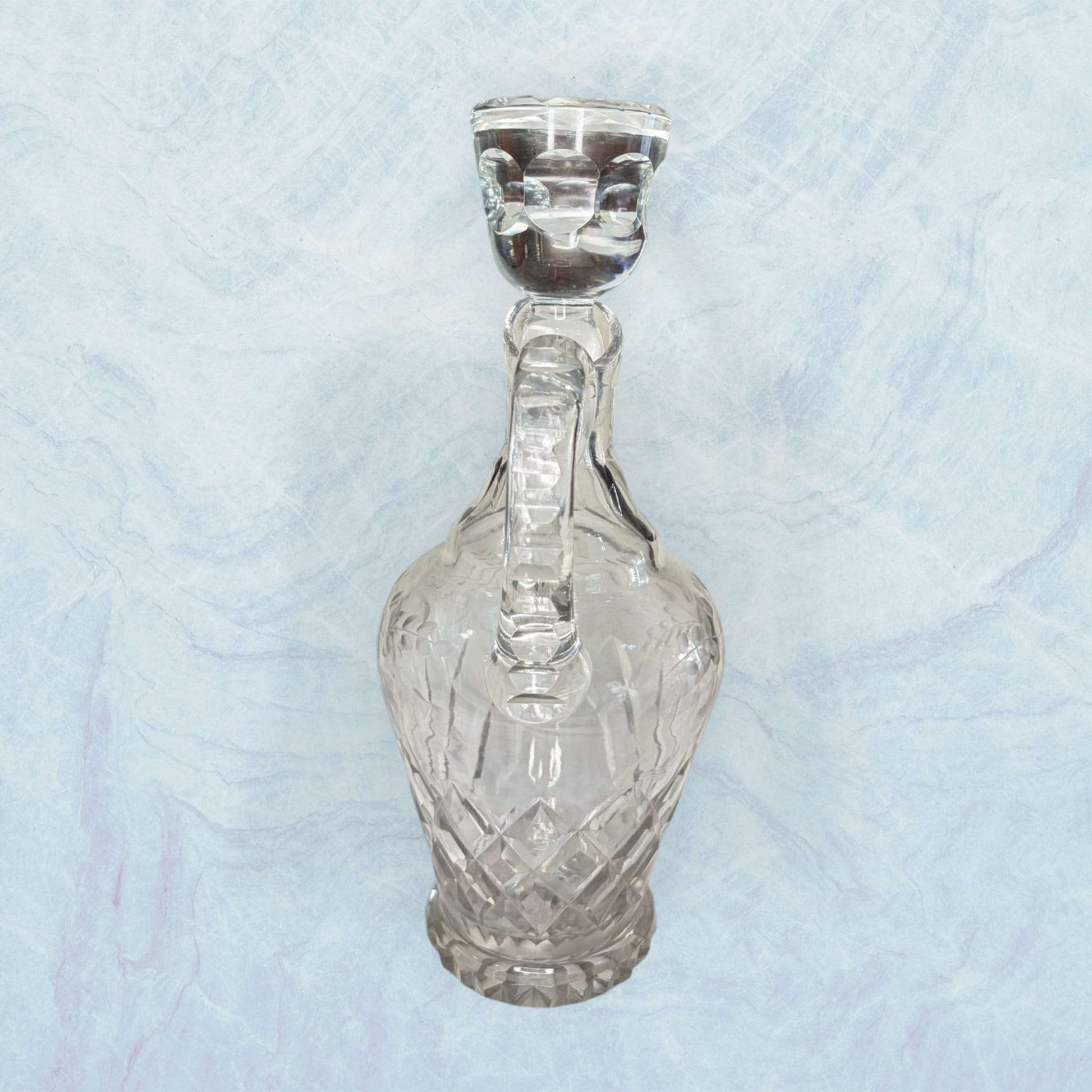 Estas Vinajeras destacan por su cuerpo de cristal transparente, con forma abombada, cuello estrecho, pico vertedor curvado y asa lateral.