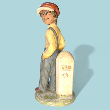 La figura “Niño Viajero” (Wanderer Boy) de Lladró representa a un joven caminante apoyado en un hito de carretera marcado con la inscripción “N-330”, evocando el espíritu aventurero, la nostalgia de los viajes y la sencillez de la vida rural.

